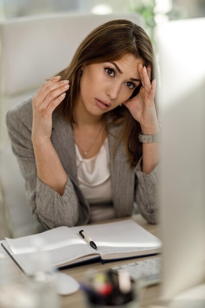 혼자 앉아서 걱정스럽게 컴퓨터를 보면서 스트레스를 받는 매력적인 젊은 비즈니스 여성.