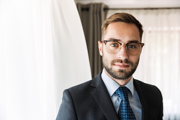 Attractive young businessman wearing suit standing at the hotel room