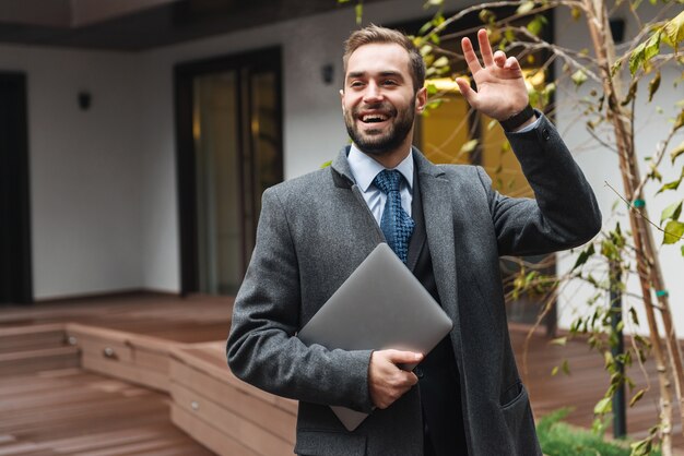 Attractive young businessman wearing suit walking outdoors, carrying laptop computer