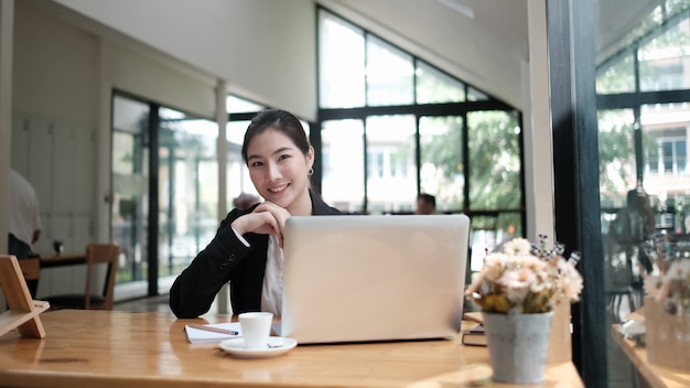 그녀의 직장에 앉아서 카메라를보고 매력적인 젊은 사업가