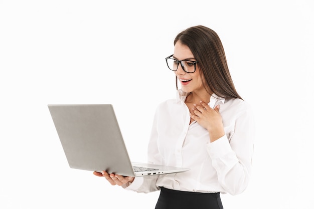 Attractive young businesswoman standing isolated over white wall, holding laptop computer