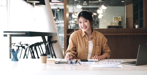 Attractive young businesswoman using calculator and smiling at camera while working in officexA