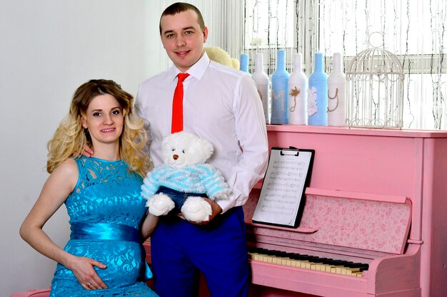 Attractive young couple is celebrating holiday at home A man and his pregnant wife stand by a piano