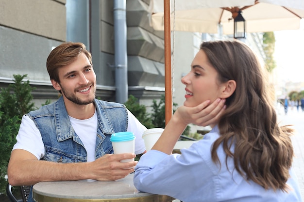 Photo attractive young couple in love drinking coffee while sitting at the cafe table outdoors.