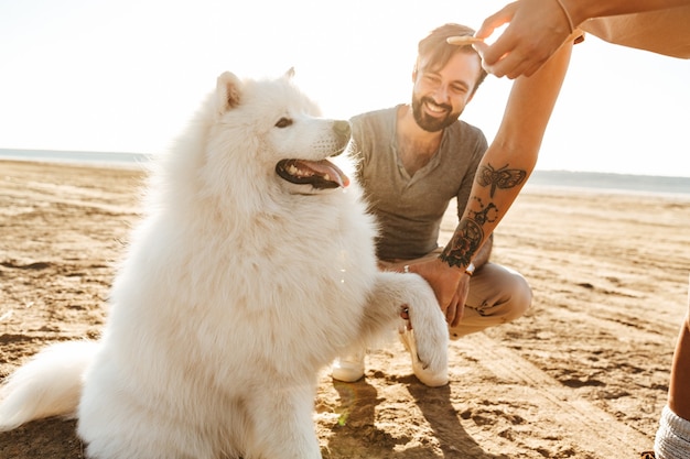 Attraente giovane coppia che gioca con il loro cane sulla spiaggia soleggiata