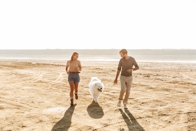 Привлекательная молодая пара играет со своей собакой на солнечном пляже
