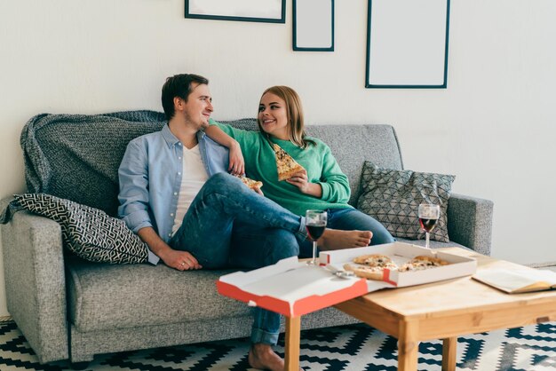 Attractive young couple relaxing on sofa eating pizza