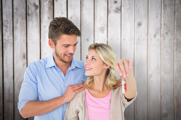 Привлекательная молодая пара показывает новый ключ от дома на фоне деревянных досок