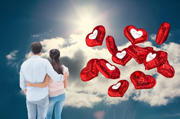 Attractive young couple standing with arms around against blue sky with clouds and sun