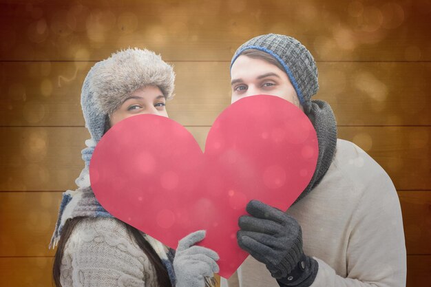 Attractive young couple in warm clothes holding red heart against black abstract light spot design