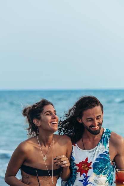 Photo attractive young couple with alcohol cocktails walking on the beach