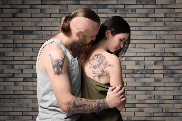 Photo attractive young couple with tattoos on brick wall background