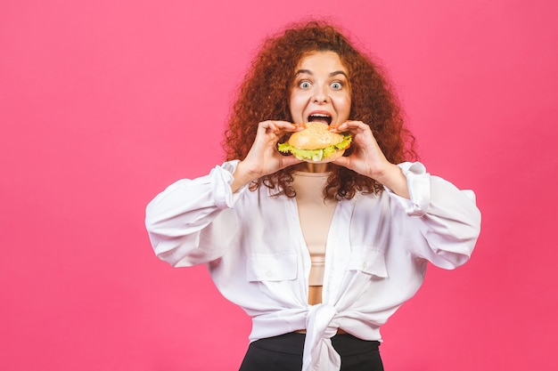 Attraente giovane donna caucasica riccia holding e mangiare un grande hamburger