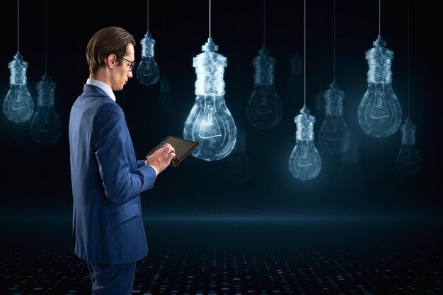 Attractive young european businessman using smartphone with\
glowing digital lamp hologram on dark background idea innovation\
and future concept