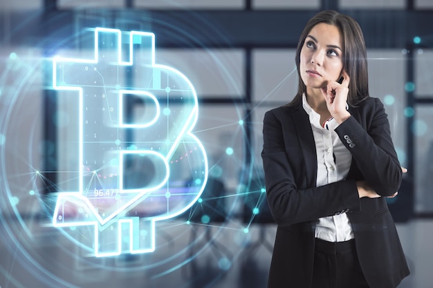 Attraente giovane donna d'affari europea con ologramma bitcoin luminoso su sfondo sfocato dell'interno dell'ufficio criptovaluta metaverse e concetto di crittografia doppia esposizione