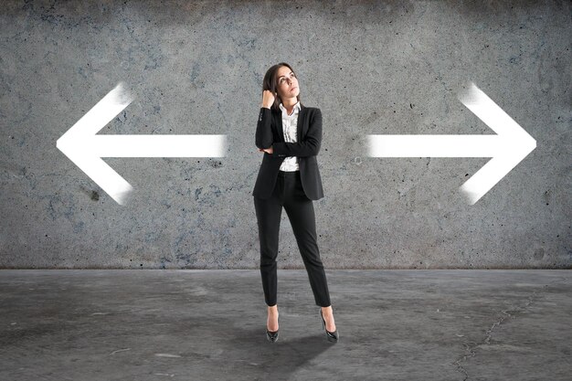 Photo attractive young european businesswoman with two arrows in concrete interior different direction and choice concept