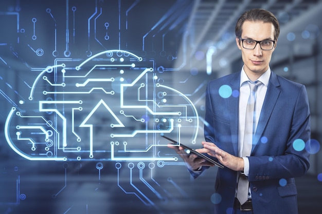 Attractive young european man using tablet with abstract glowing circuit cloud hologram on blurry office interior background Big data and technology concept Double exposure