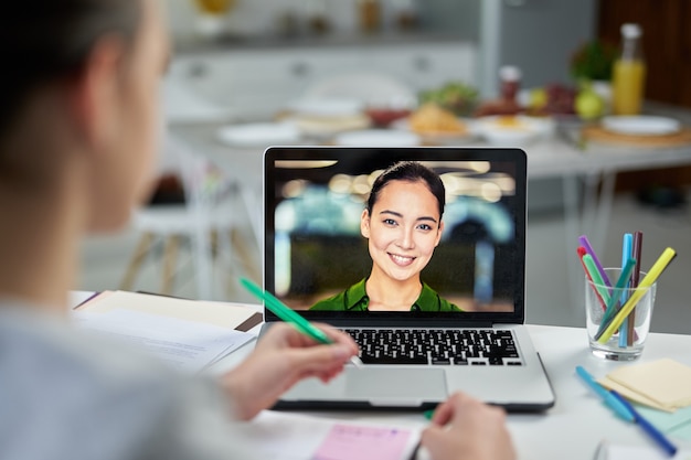 Attractive young female teacher smiling to her students, using video chat app during online lesson. Home schooling during quarantine. Focus on laptop screen