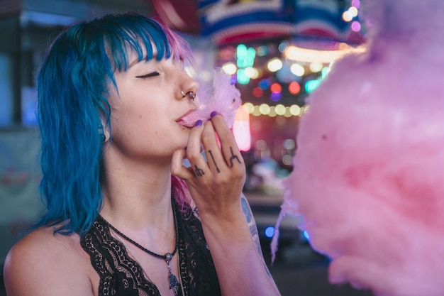 Attractive young female with blue and pink hair eating cotton candy in an amusement park