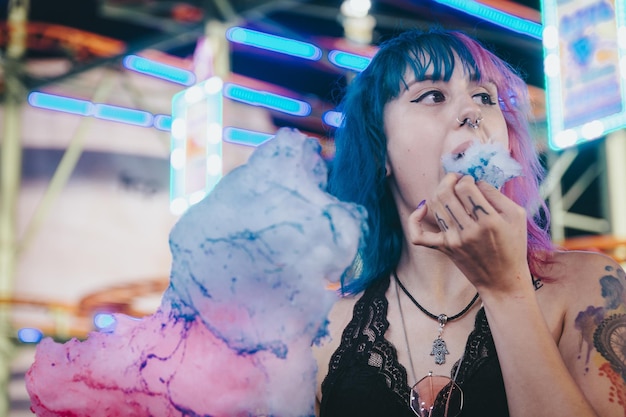 Attractive young female with blue and pink hair eating cotton candy in an amusement park