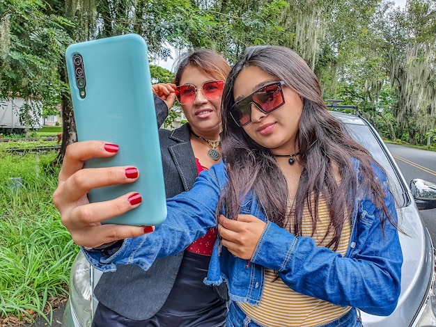 Attractive young females taking a selfie in front of their car in the park