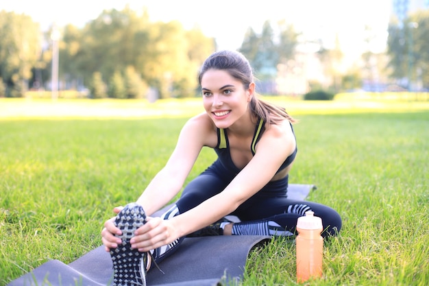 Attractive young fitness woman exercising outdoors, stretching exercises.