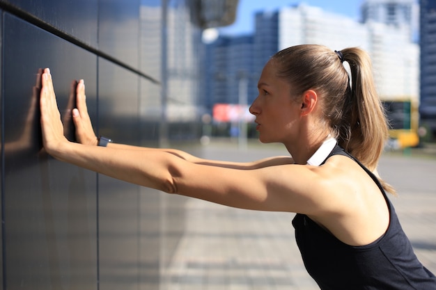 屋外で運動するスポーツウェアを着て、ストレッチ運動をする魅力的な若いフィットネス女性。