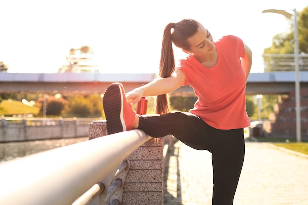 Attractive young fitness woman wearing sports clothing exercising outdoors, stretching exercises.