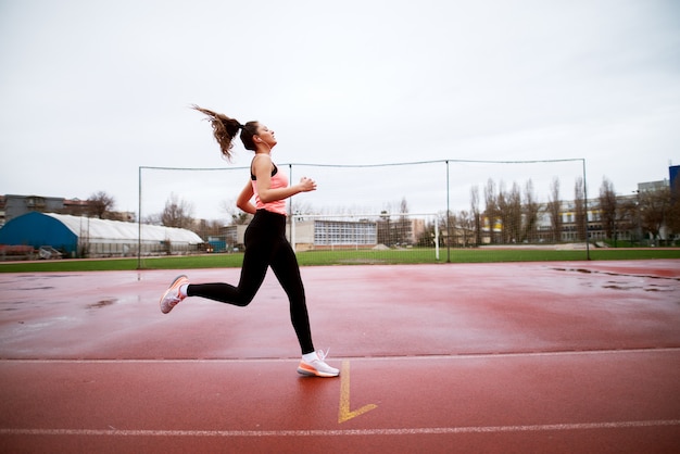 Attractive young focused fitness girl arriving at the finish line after sprint near the soccer field.