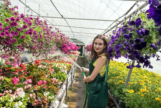 Attractive young gardener everyday taking care plants with a watering can in a greenhouse. occupation in hothouse