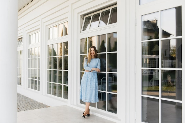 Attractive young girl on the background of the white house in a blue dress