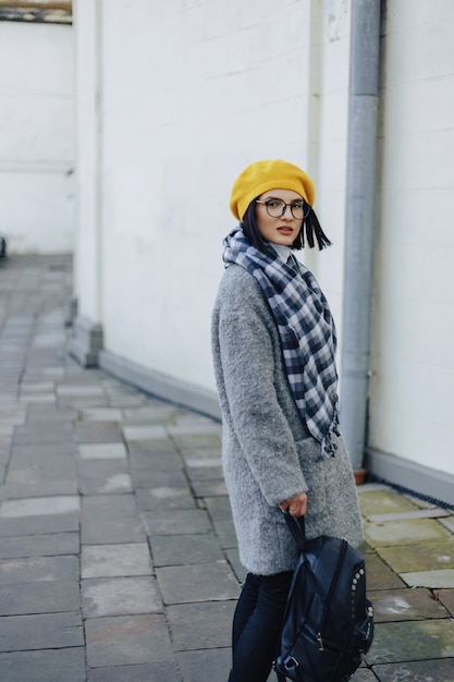 Attractive young girl in glasses in coat and yellow Beret freestyle walking