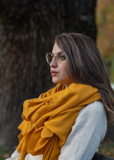 attractive young girl in glasses with big beautiful eyes sits on a bench in an autumn park