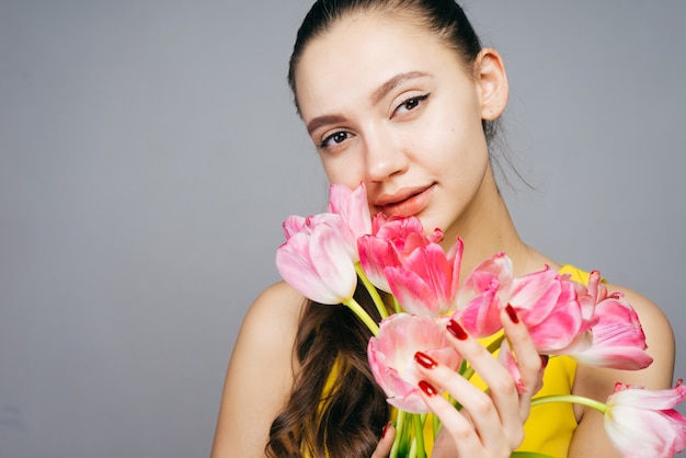 ピンクの花の花束を持って、カメラを見て魅力的な若い女の子