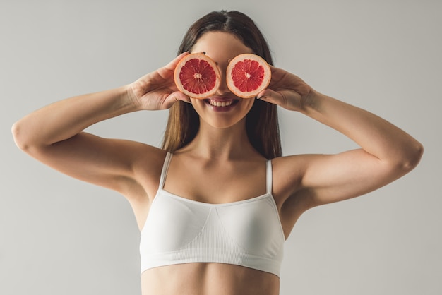 Attractive young girl is holding slices of grapefruit.