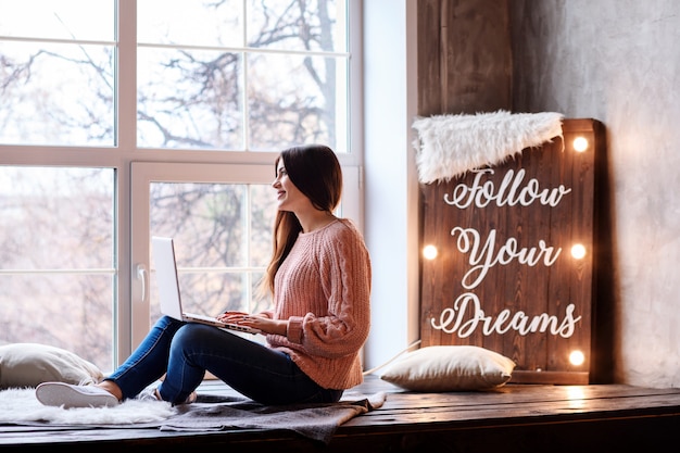 Photo attractive young girl is working or studying at home using her laptop. follow your dreams motivation lettering written on the lightboard.