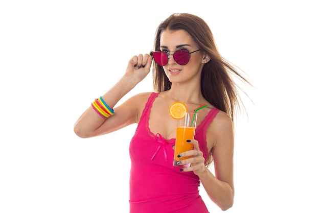 Attractive young girl in pink shirt and sunglasses drink orange cocktail isolated on white background