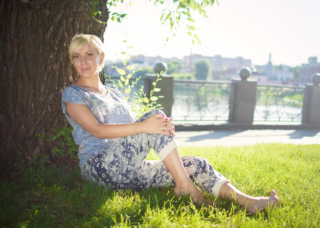 Attractive young girl sits in a park near a tree