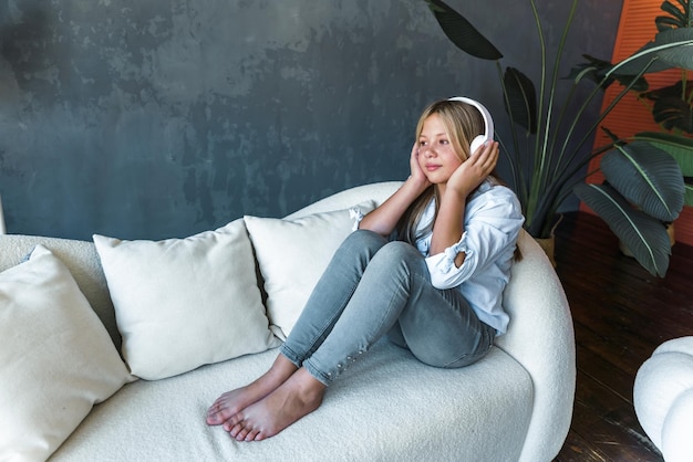 Attractive young girl on the sofa at home she plays music on her smartphone and headphones the concept of relaxation and entertainment