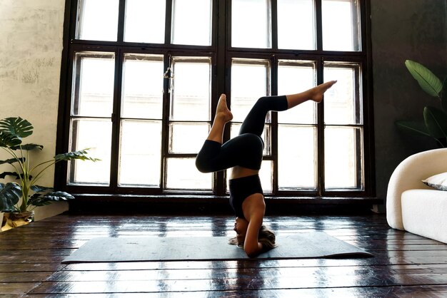 Attractive young girl stands on her head and upside down and does fitness at home