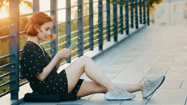 Attractive young girl teenager pretty redhead woman with short hair sit on city bridge rest outdoors