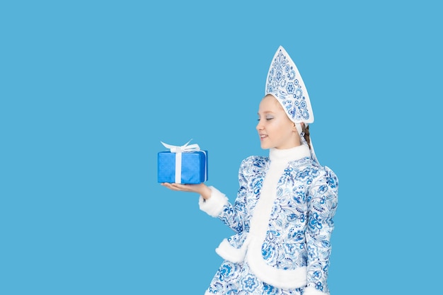 Attractive young girl wearing blue suit of snow maiden holding gift box. Isolated on blu background