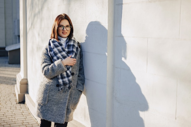 Attractive young girl wearing glasses in a coat walking on a sunny day