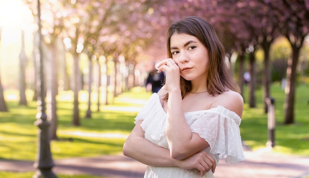 Attractive young girl in a white dress stands in a blooming park