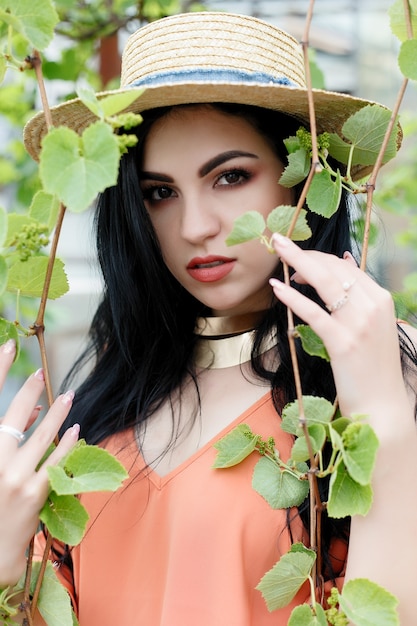 Attractive young girl with wavy hair wearing hat and stylish outfit posing near the vine