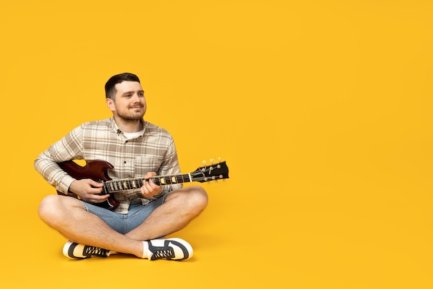 Привлекательный молодой парень с гитарой в руках на желтом фоне