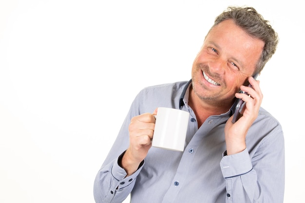 Привлекательный молодой красивый мужчина-бизнесмен счастливо улыбается с чашкой кофе во время разговора по смартфону