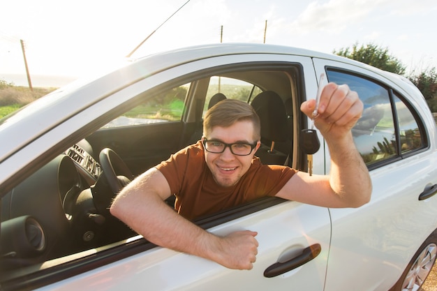 彼の新しい車のキーを見せて笑っている魅力的な若い幸せな男。