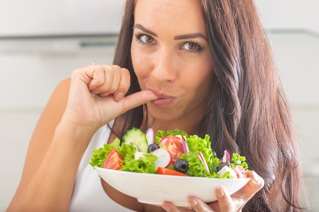 野菜サラダを食べる魅力的な若くて幸せな女性。