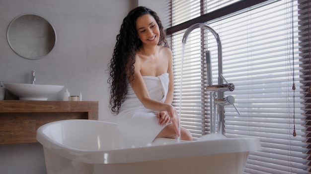 Attractive young happy woman taking bath washing hands under running hot water pretty smiling girl